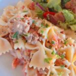Creamy sausage tomato bowtie pasta with bacon avocado salad on white plate