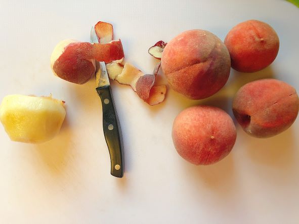 Peeling fresh peaches with knife on white cutting board