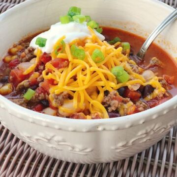 taco soup in bowl from side with cheese sour cream green onion toppings