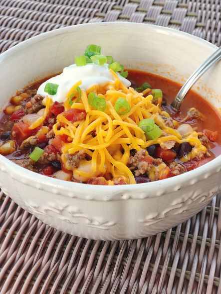 taco soup in bowl from side with cheese sour cream green onion toppings