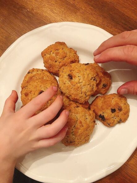 hands grabbing oatmeal raisin cookie off white plate