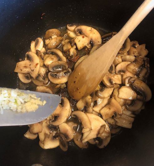 adding minced garlic to sauteed sliced mushrooms