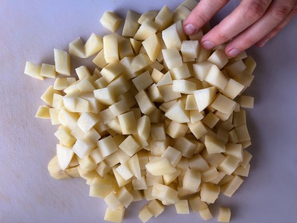 diced potatoes on cutting board with hand to show scale