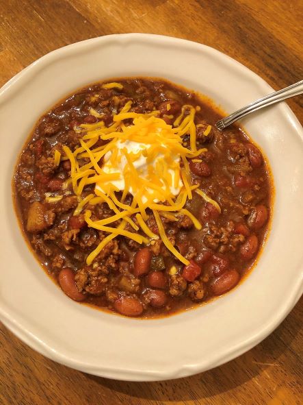 curry chili in bowl topped with sour cream and shredded cheddar cheese