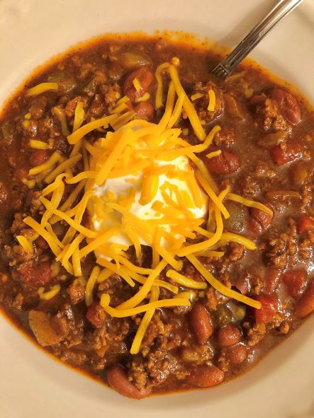 curry chili in a bowl topped with sour cream and shredded cheddar cheese