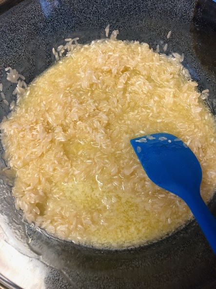 stirring uncooked white rice with melted butter