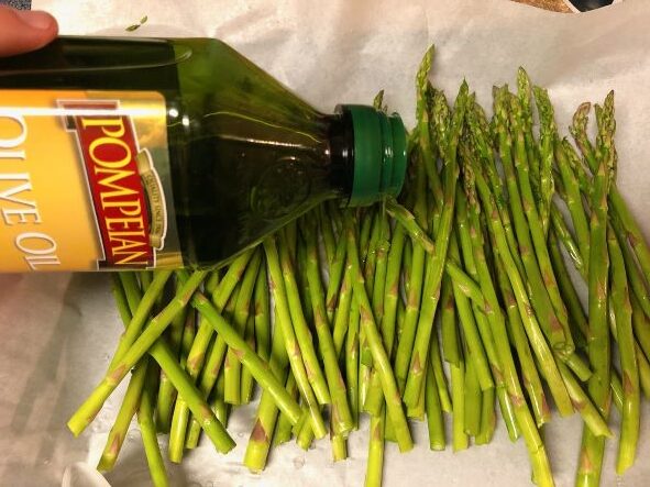 pouring olive oil over fresh asparagus