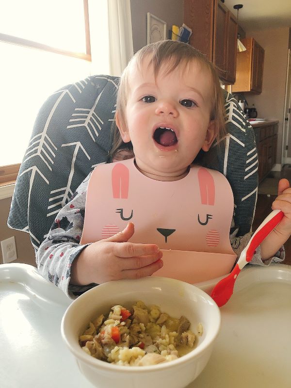 baby eating chicken noodle soup in high chair