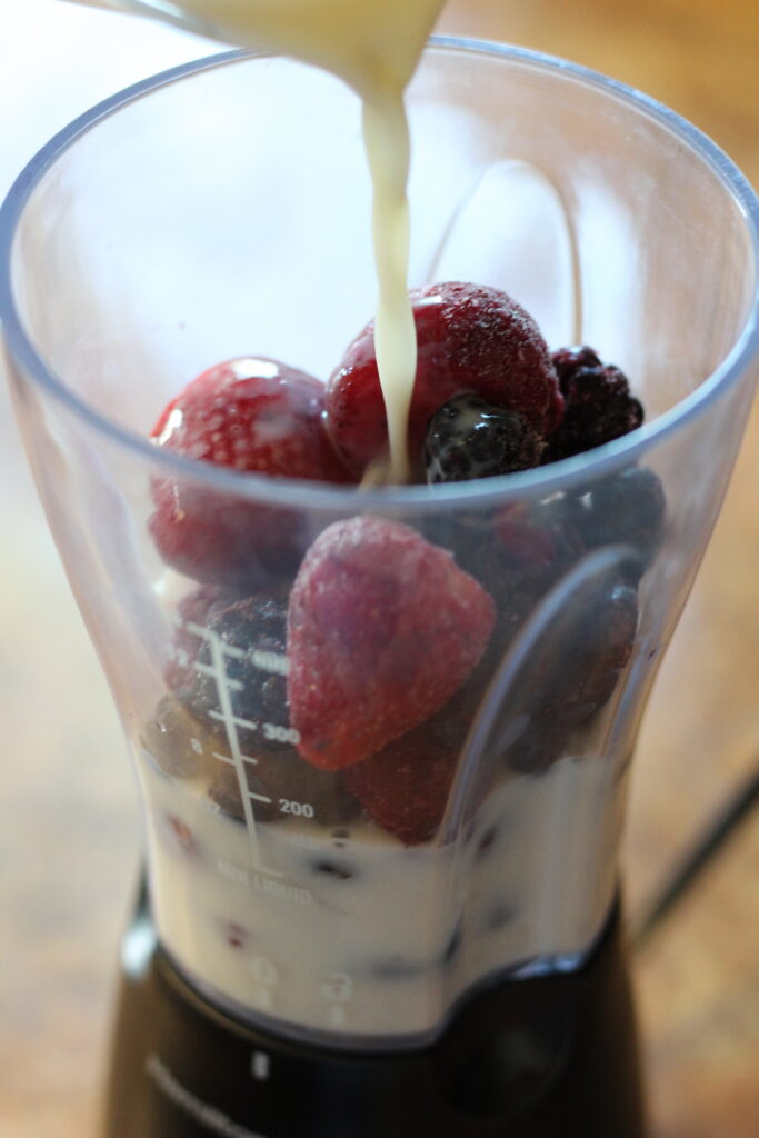 pouring milk over berries for smoothie
