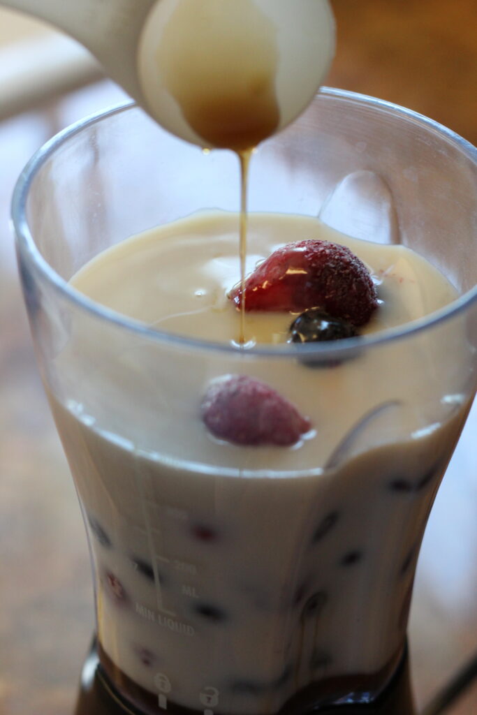 drizzling maple syrup over berries and milk for smoothie