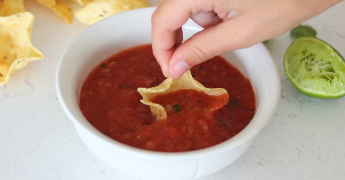 fresh Chili's inspired salsa in white bowl with scooping, lime and tortilla chips